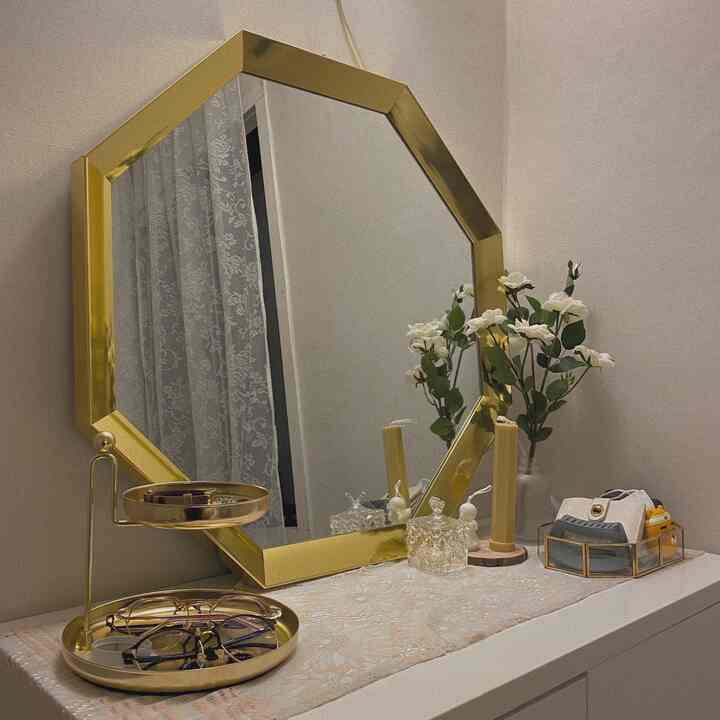 ゴールドフレームの鏡とゴールドトレイ、白いドレッサー上に花とキャンドルが置かれた雰囲気あるパウダールームのインテリア