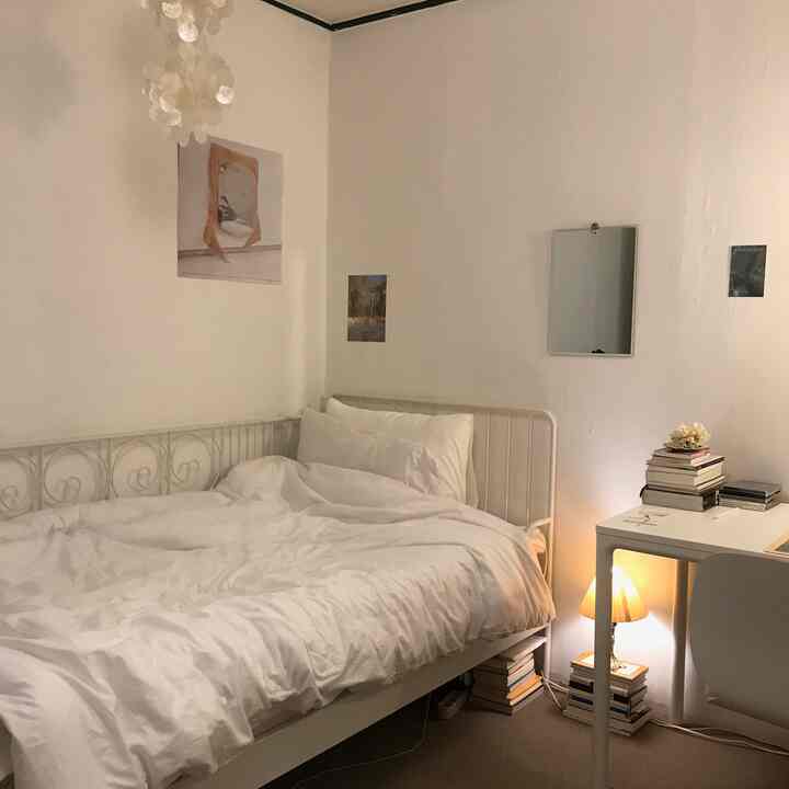 Soft white-toned bedroom featuring a metal bed frame, desk, and mirror, creating a simple and cozy atmosphere