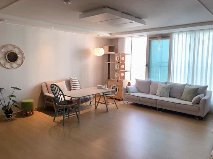 A natural-tone living room with white walls, beige sofa for 4-person household, wooden floor, and a cat tower near window