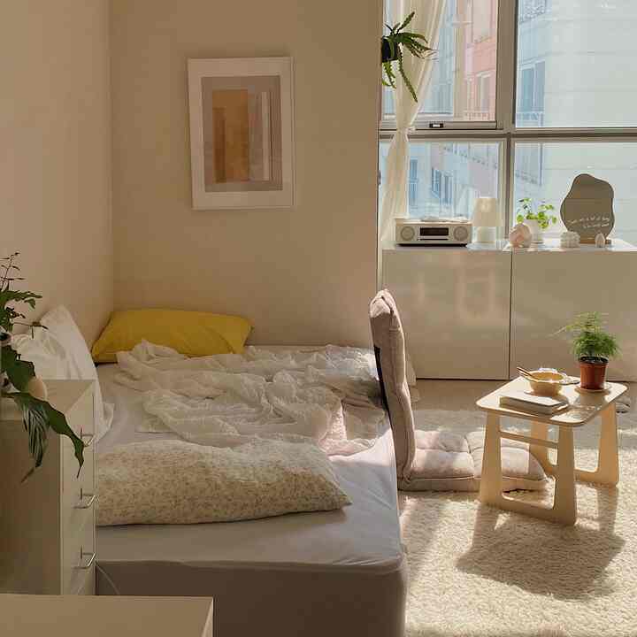 暖かいホワイトトーンの寝室、座椅子と小さなナチュラルウッドテーブルが配置された雰囲気のあるインテリア