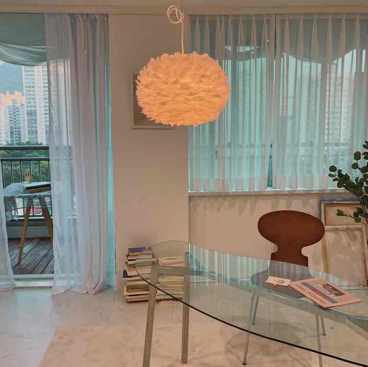 Bright toned living room featuring glass table, wooden chair, and pendant lighting in a natural modern style space