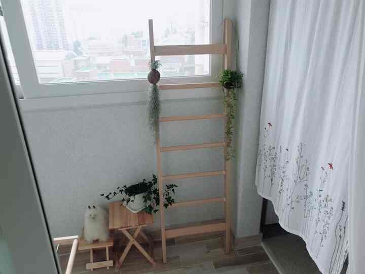 Bright natural-toned veranda featuring a wooden drying rack, embroidered curtains, and various plants creating a cozy atmosphere