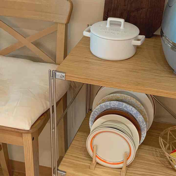 Natural wood tone kitchen featuring a wooden shelf, IKEA chair, and neatly arranged plate rack creating a cozy and tidy atmosphere