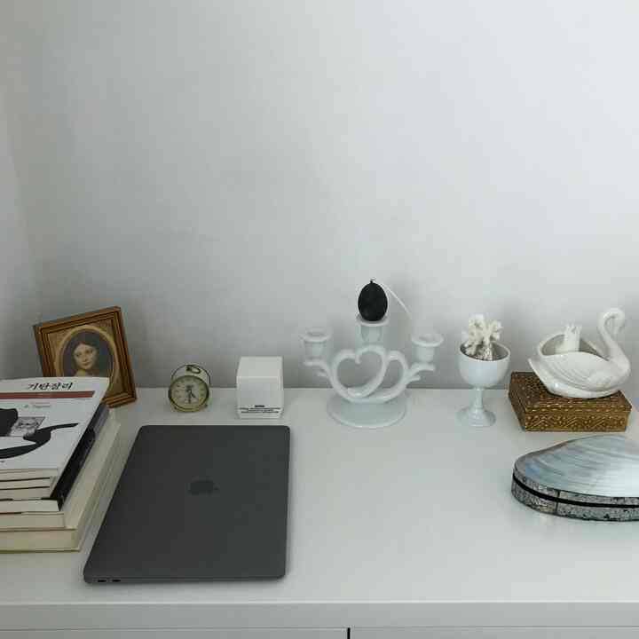 ホワイトトーンのキャビネット上にラップトップ、ゴールドの時計、オブジェが置かれた清潔感のあるホームオフィス空間