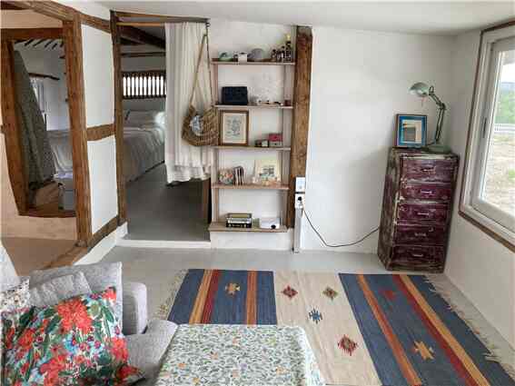 A simple living room with natural white walls and wooden furniture, featuring a sofa with floral cushions and a colorful patterned rug