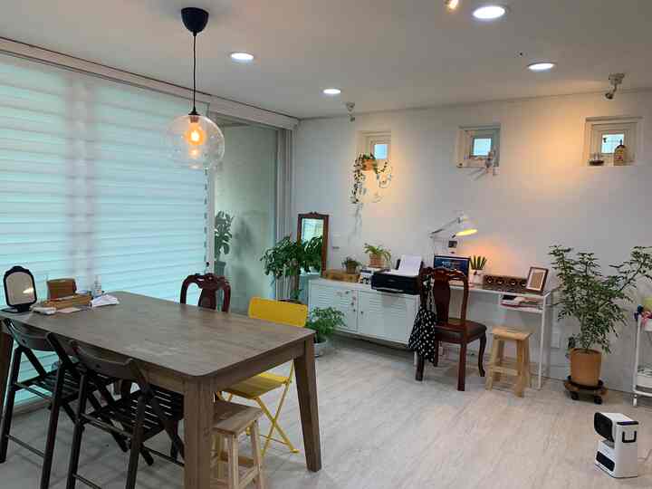 Bright white and wood tone workspace featuring a dining table, chairs, and various plants creating a natural atmosphere