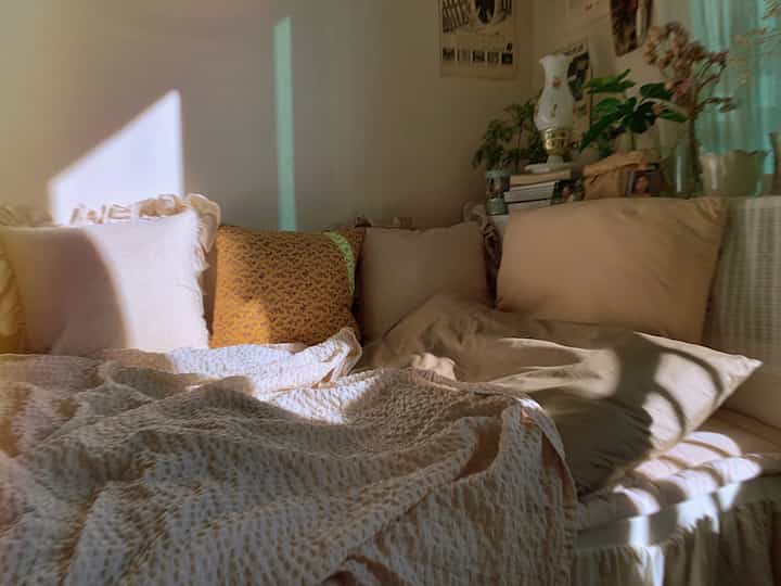 Warm beige bedroom with sunlit sofa featuring cushions and cozy bedding