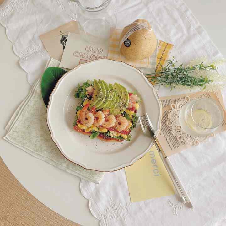 White and yellow toned home cafe setting featuring an open sandwich and elegant plate on a cozy dining table