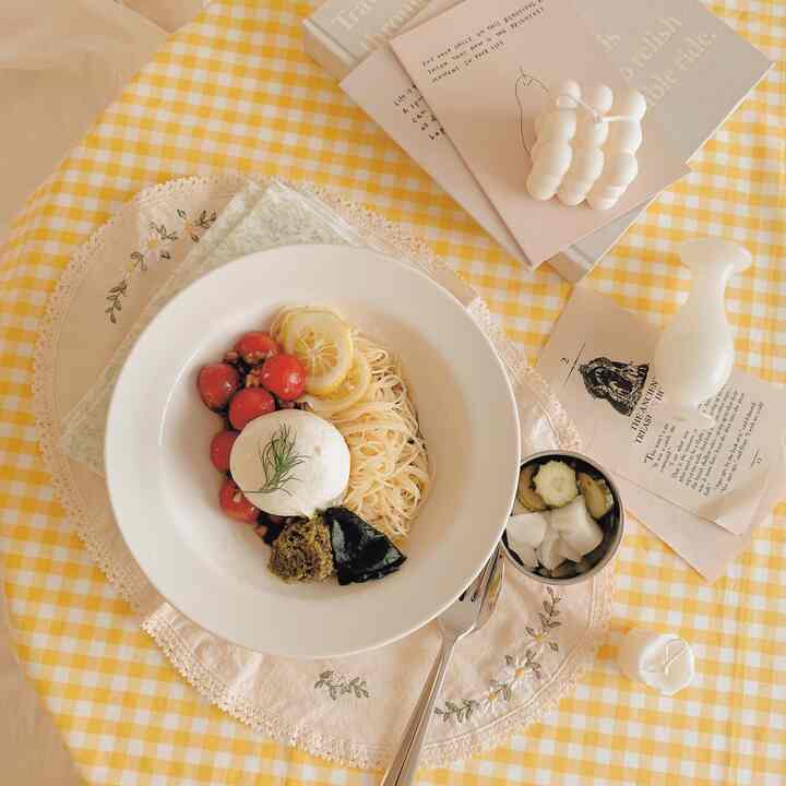 Yellow check round table featuring a white plate with burrata cheese summer pasta in a cozy home cafe setting