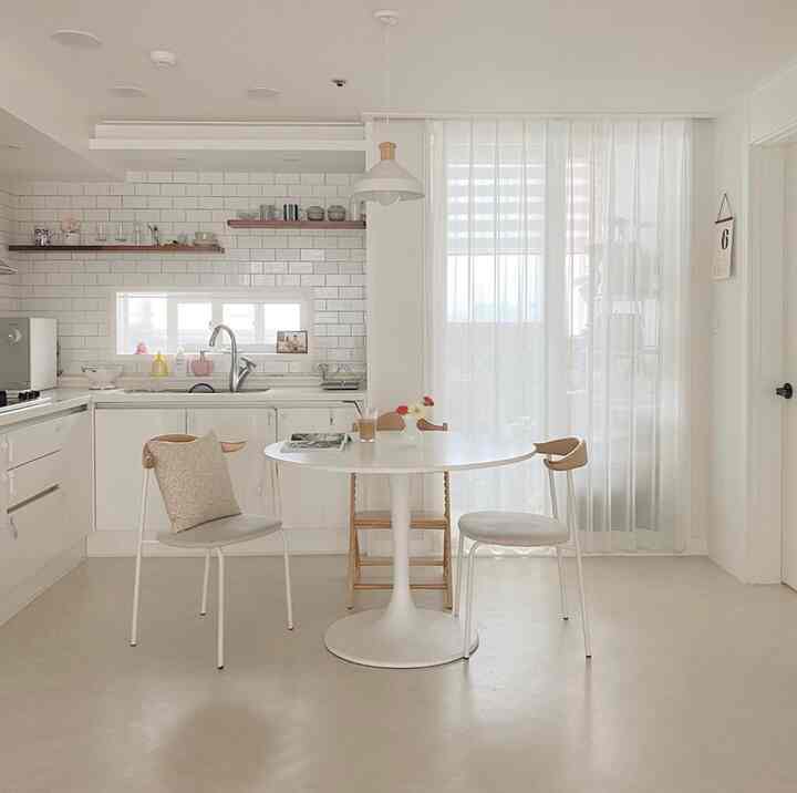 White and natural wood tone kitchen featuring round dining table and metal chairs, creating a clean and peaceful atmosphere