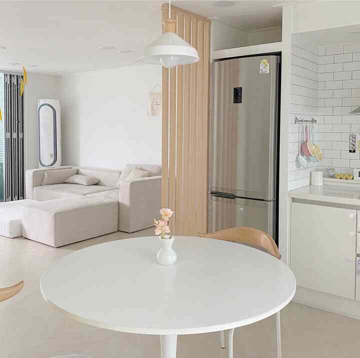 White and wood tone kitchen and living room with round dining table and wood room divider creating cozy atmosphere