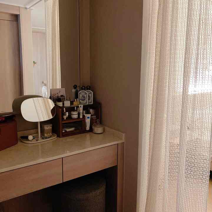 A neat powder room featuring ivory curtains and a natural brown vanity with organized cosmetics