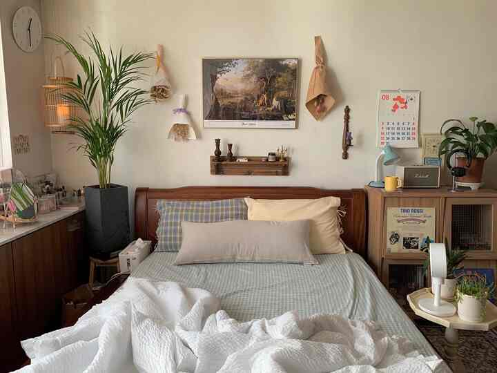 A cozy bedroom with natural wood tones and beige, light green bedding; the wall features a picture frame and dried flower decor