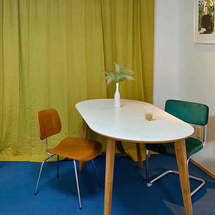 Compact dining area with bright yellow curtain and blue rug, featuring white oval dining table with wooden legs and two different chairs