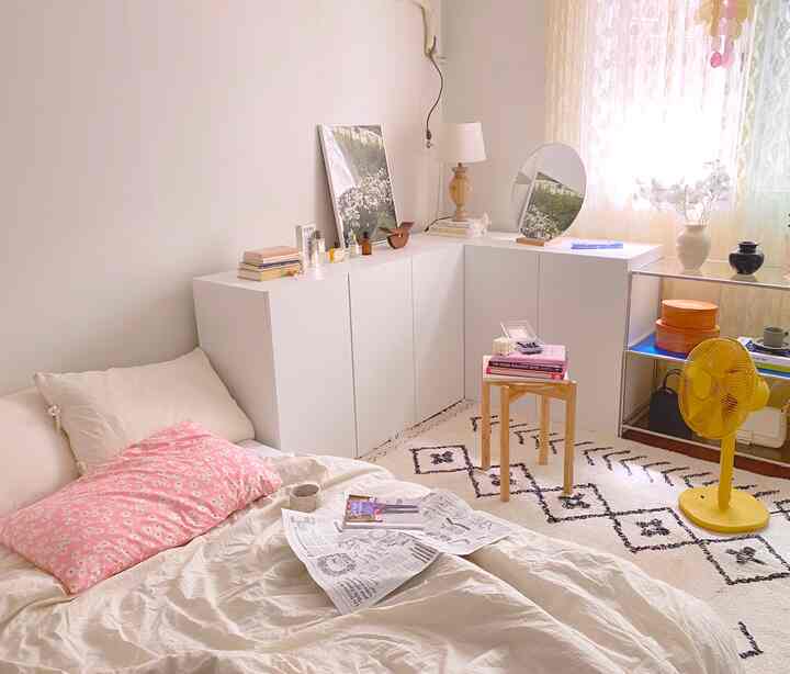 White and natural wood tone studio bedroom featuring storage cabinets, patterned rug, and wooden stool with cozy ambiance