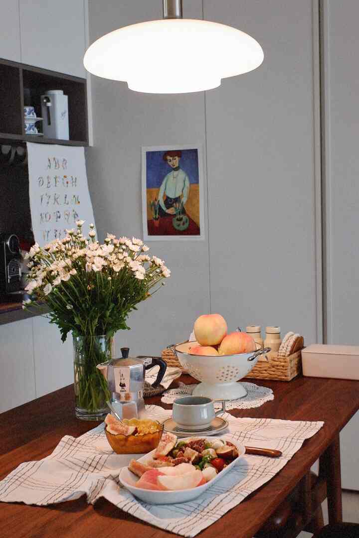 White walls and wooden dining table featuring a vase of chrysanthemums and coffee items in a natural, minimal dining space