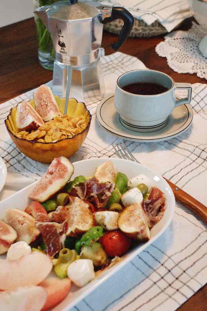 温かみのある木製のテーブルの上に、モカポット、コーヒーカップ、新鮮なイチジクをのせたサービングディッシュが配置された居心地の良いダイニング空間