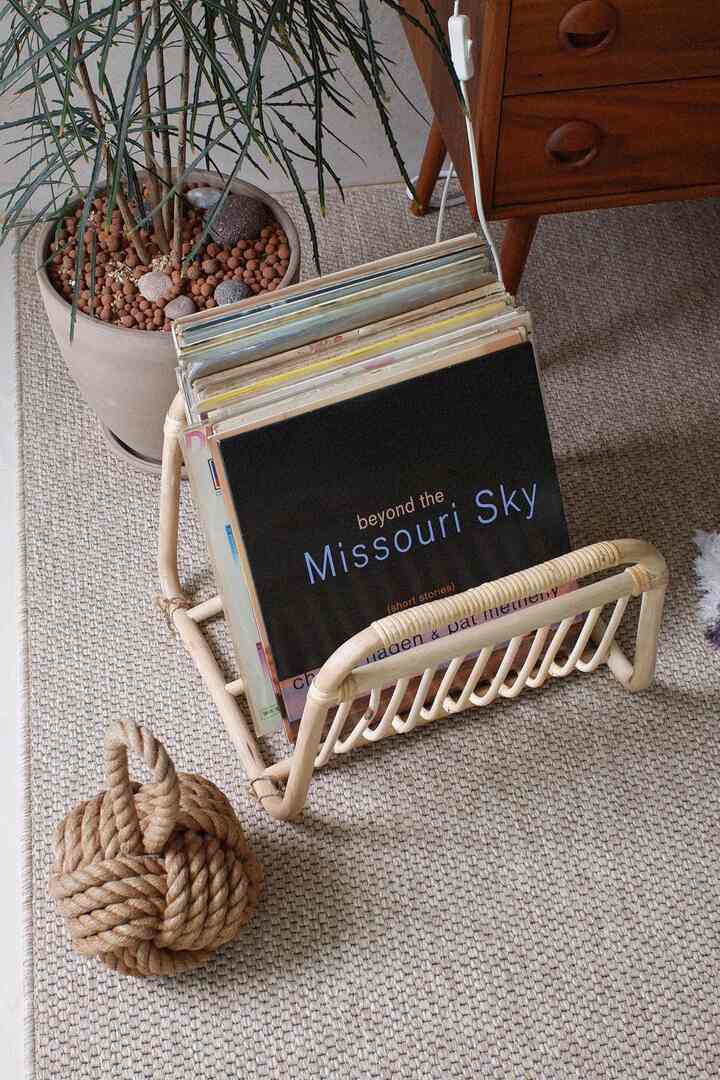 Beige rug featuring a natural-toned magazine rack with brown rope door stopper and partial nightstand visible in a living room setting