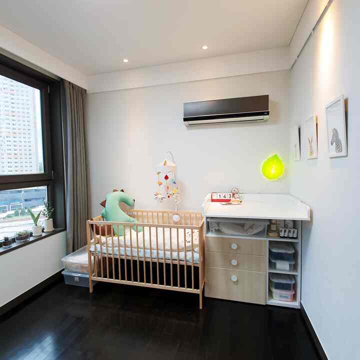 白い壁と木目調家具が調和した赤ちゃんの部屋、ベビーベッドとおむつ交換台が配置され、窓から自然光が入る落ち着いた空間
