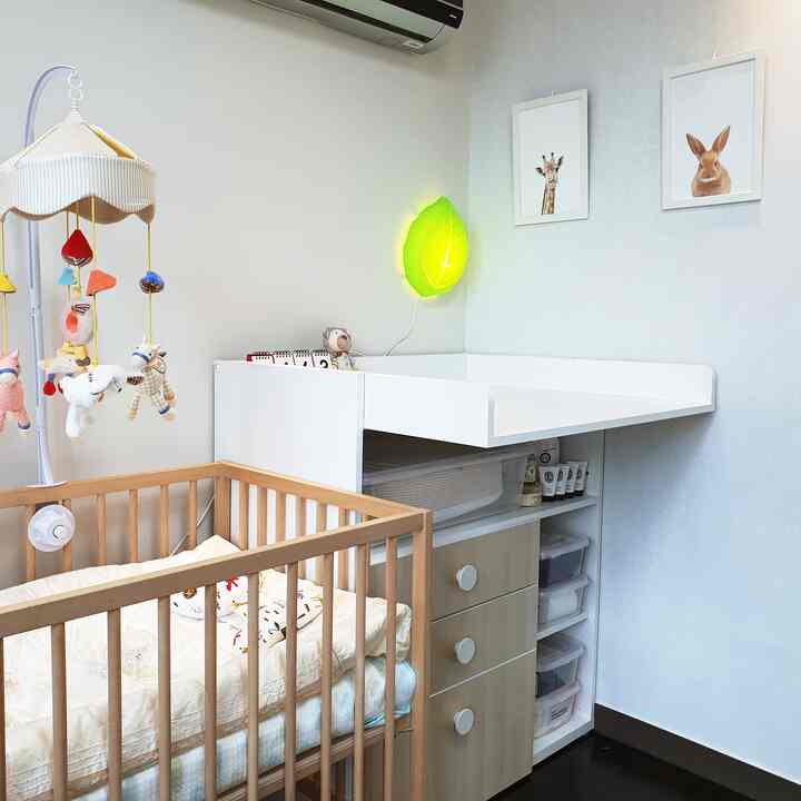 白とナチュラルカラーの赤ちゃん部屋、木製ベビーベッドとおむつ交換台、葉っぱの形の壁照明が配置された印象的な空間