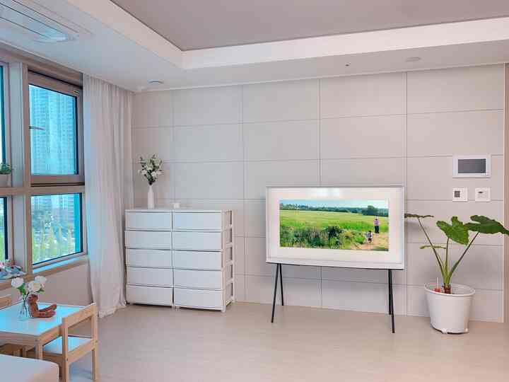 Bright white-toned living room featuring a child-sized table and chairs, TV on stand, and dresser, with a natural and clean atmosphere