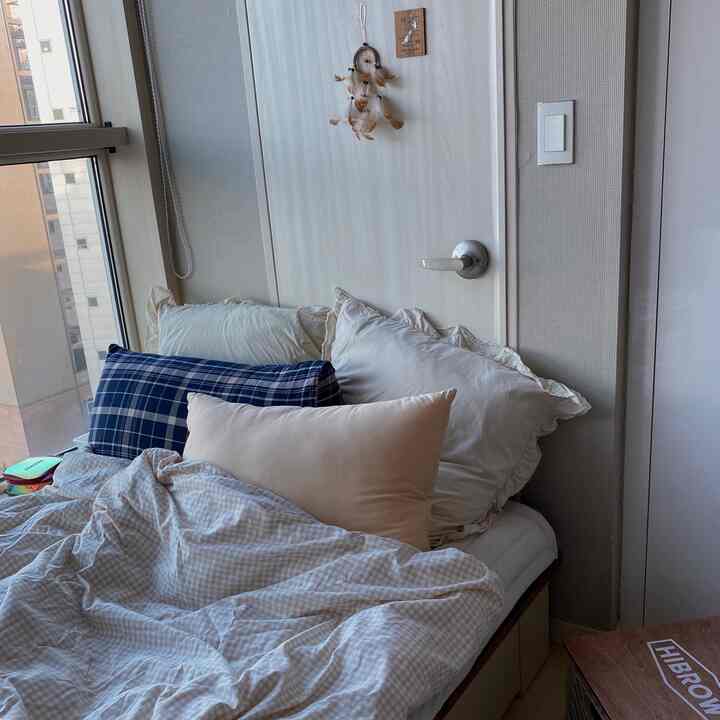 柔らかいベージュトーンの寝室、複数の枕とベッドリネンが配置された雰囲気のあるワンルームの寝室