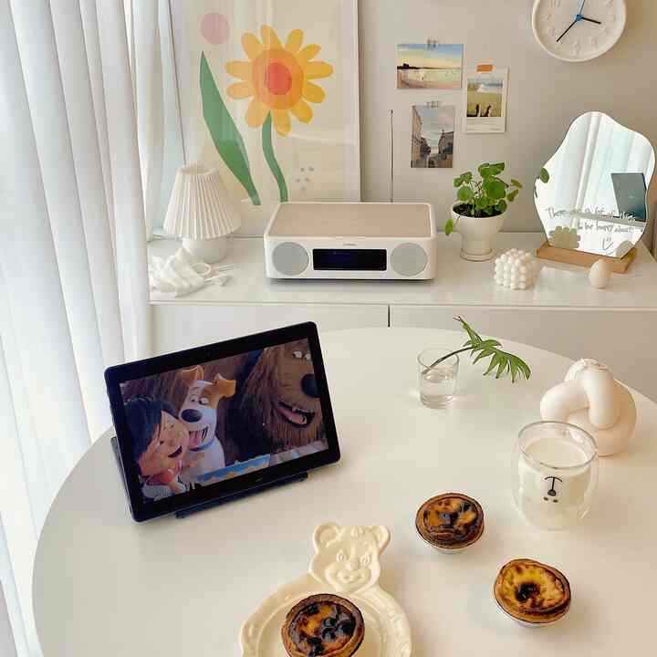 Soft white-toned living room featuring a round table, white cabinet, posters, and plants creating a cozy atmosphere