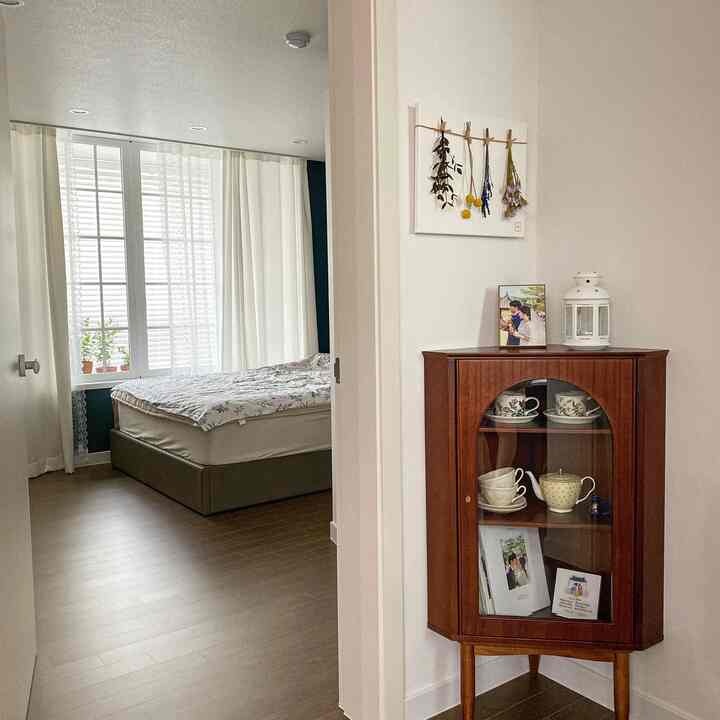 White and brown toned bedroom featuring a corner cabinet, blackout curtains, and summer bedding creating a clean natural atmosphere
