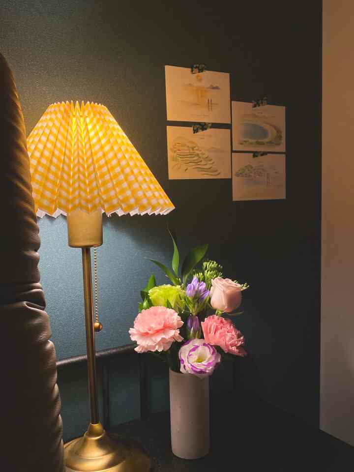 Warm-toned bedroom corner with yellow checkered pleated shade table lamp and a vase of colorful flowers