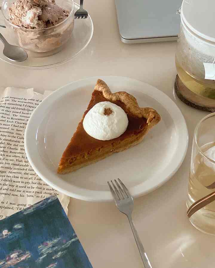 Warm beige-toned table featuring pumpkin pie slice, ice cream in a glass bowl, and clear teacup in a cozy home cafe setting