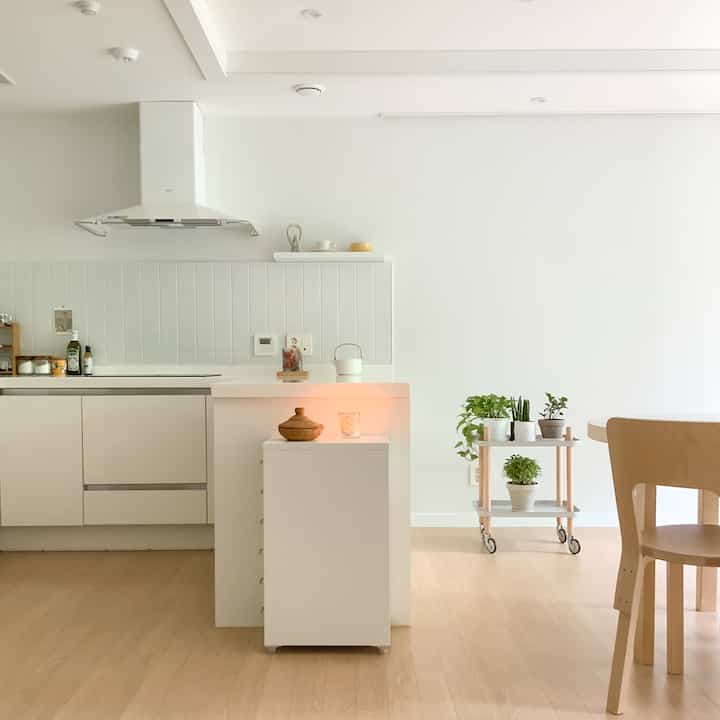 明るい白壁と木目調の床が特徴的なワンルームのキッチンとリビング、シンプルで自然な植物とキャンドルが置かれた雰囲気のあるインテリア