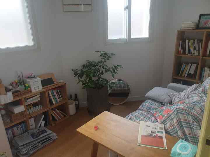 Bright white-walled small living room with wood flooring, featuring a plaid sofa and a bookshelf creating a cozy atmosphere