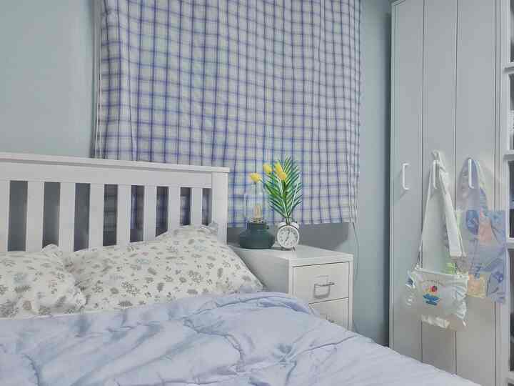 Sky blue and white toned bedroom with blue check curtain, white wooden bed frame, nightstand creating a fresh and cozy space