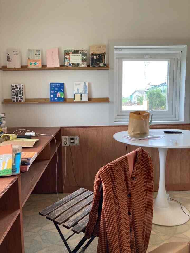 White walls and wood-toned furniture in a writer's room featuring a desk, folding chairs, and a round table by a window, creating a cozy space