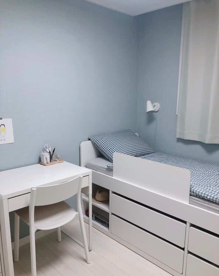 白と青のトーンの子供部屋、ミニマルな家具と収納付きベッドが配置された落ち着いた雰囲気のインテリア