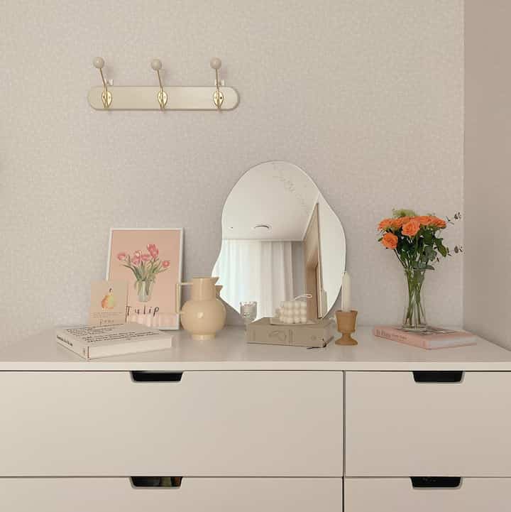 Simple room in white tones with a dresser featuring a curved mirror and vase, creating a cozy vanity space