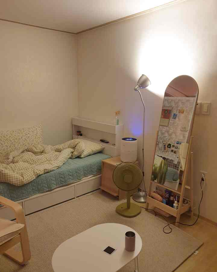 Beige and natural wood-tone studio bedroom featuring a neat bed, nightstand, full-length mirror, and fan in a cozy setting