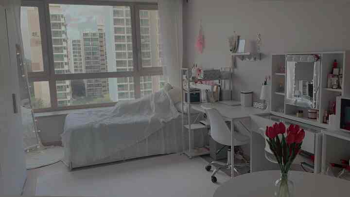 A white-toned studio bedroom featuring a bed by the window, a workspace, and a vanity, creating a clean and cozy atmosphere