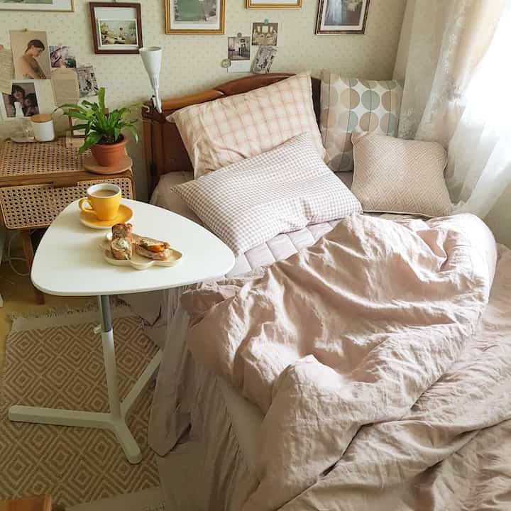 Beige and pink toned studio bedroom featuring wooden bed with cushions and cozy bedding
