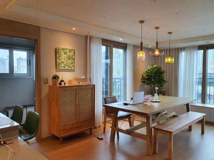 Natural wood tones and white hues define this dining room featuring a large wooden table and multiple pendant lights, creating a cozy family atmosphere