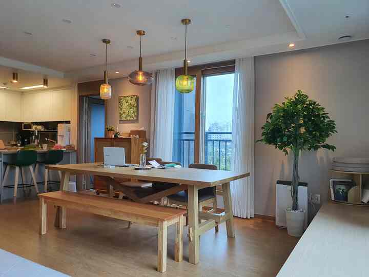 Natural-toned dining room featuring wood dining table and bench, green plants, and pendant lights creating a warm atmosphere