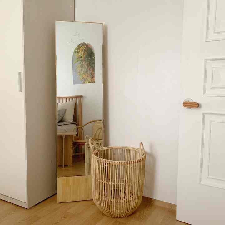 白い壁と木目調の床、ラタンバスケットと大きな全身鏡が配置された雰囲気のある寝室の一角