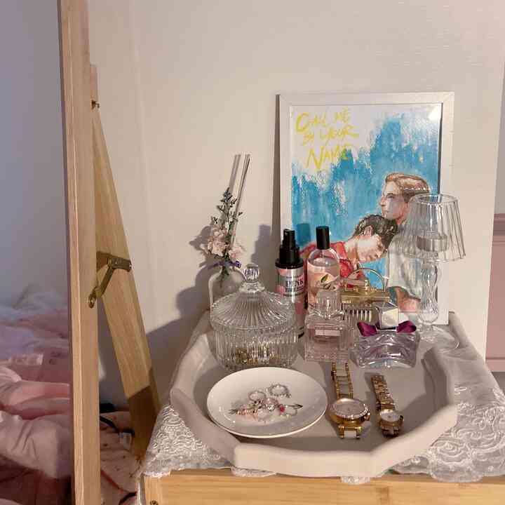 White and pink toned single household nightstand with lace tablecloth, perfumes, and watches arranged neatly in a simple setting