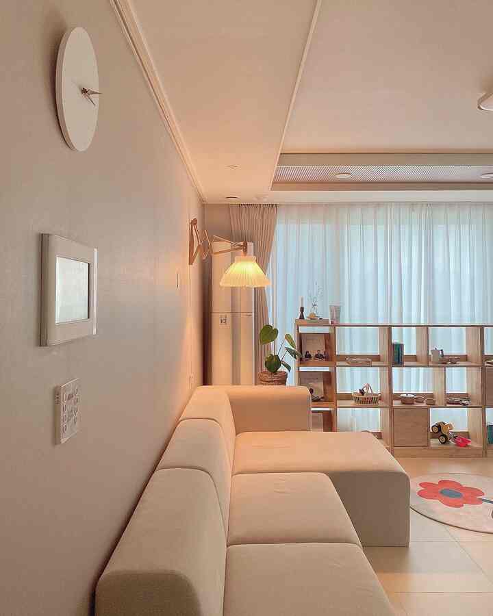 Warm beige and white toned living room featuring natural wood bookshelf and large sofa, cozy space for living with a baby