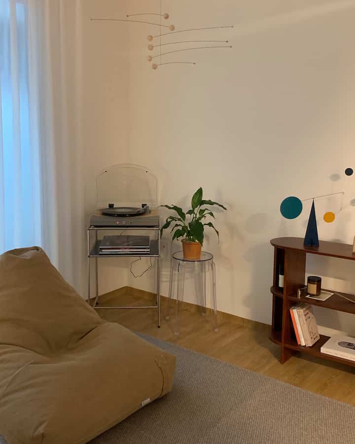 Natural colored dining room featuring a beige bean bag, transparent stool with plant, and wooden sideboard creating a cozy atmosphere
