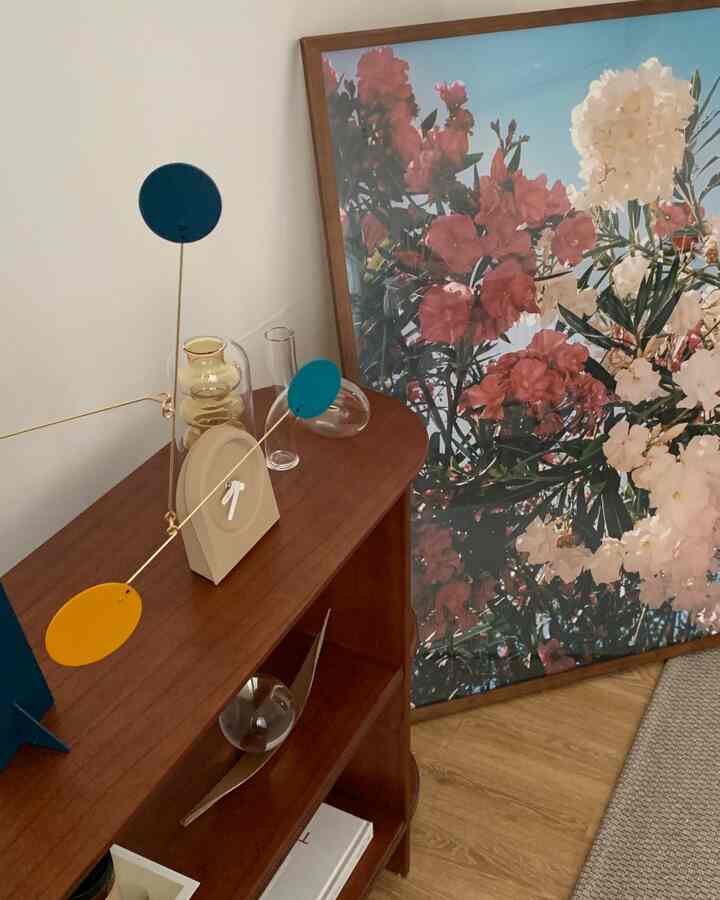 Brown-toned cabinet topped with colorful mobiles and transparent vases, alongside floral framed artwork in an emotive dining room decor setup