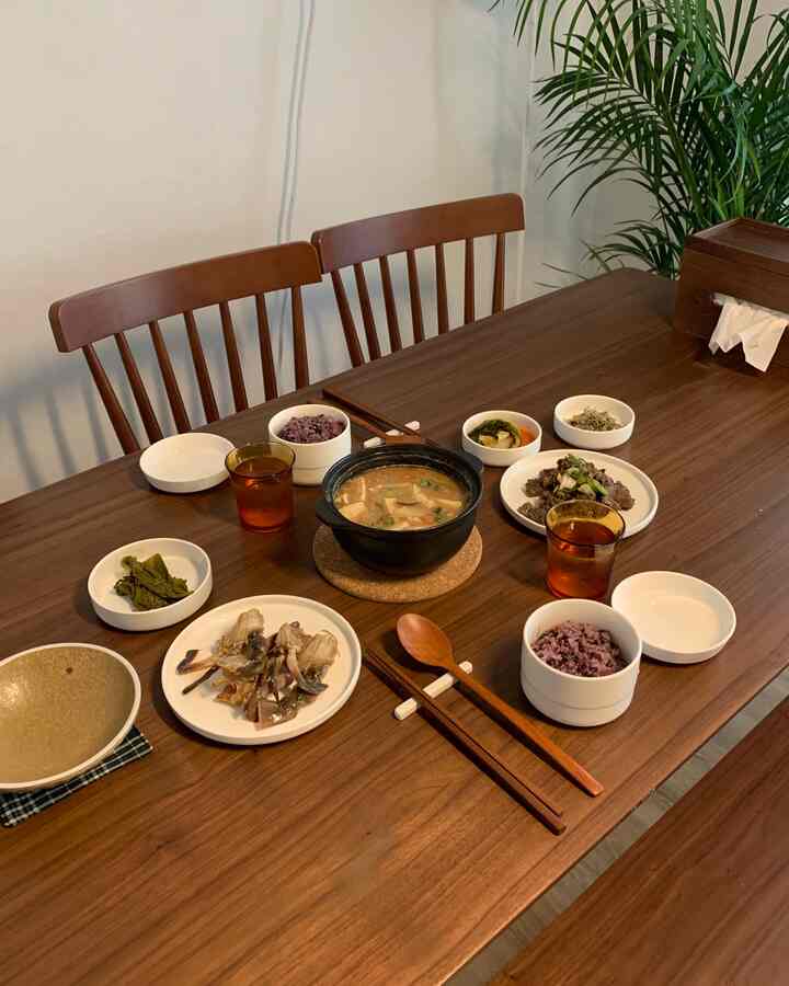 Natural brown wood tone dining room featuring a wooden dining table and Czech chairs with Korean tableware and side dishes neatly arranged