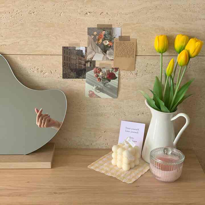 Beige wall and wooden table featuring yellow tulip vase and various decor items creating a cozy atmosphere