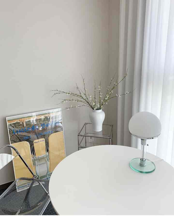 ホワイトとベージュトーンのリビング、丸テーブルと白いカーテン、陶器の花瓶が配置された清潔感のあるモダンな空間