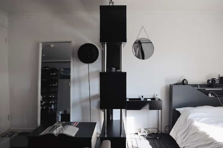 Black-toned studio bedroom featuring simple black furniture, mirrors, desk, and bed in a modern setting